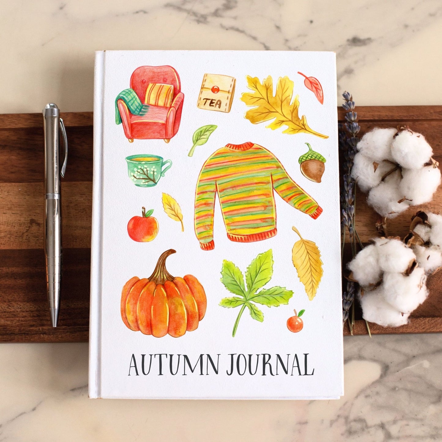 Autumn-themed notebook with illustrations of a pumpkin, sweater, and leaves on a marble surface.
